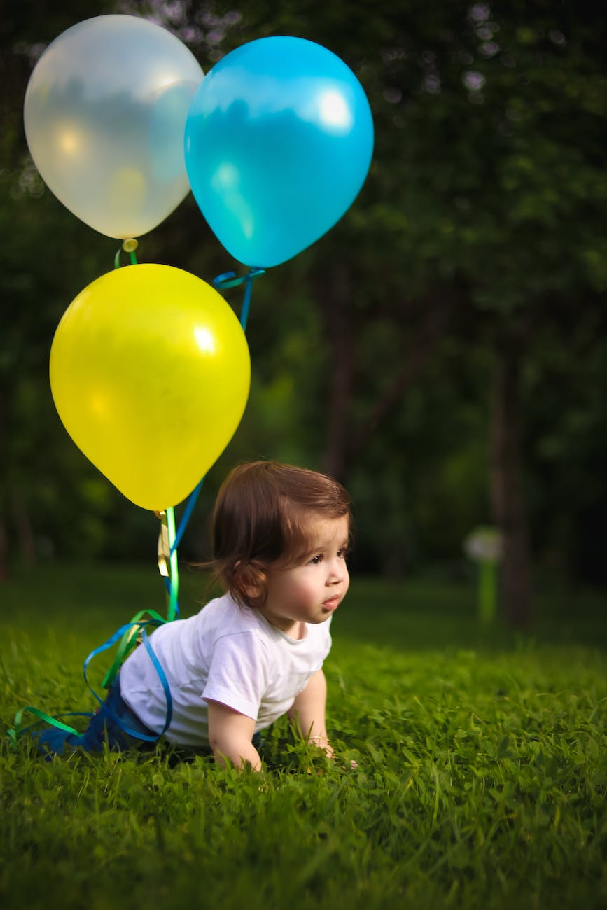 baby wearing white shirt tied with three balloons